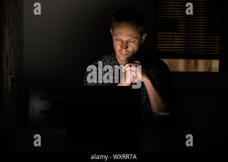 Der Mann bei der Arbeit in der Nacht ist auf der Suche nach einem Laptop Bildschirm. Stockfoto