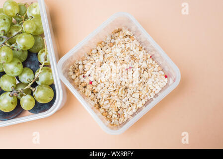 Das richtige Frühstück mit grünen und schwarzen Trauben und Getreide Müsli. Müsli und frisches Obst in einer Brotdose auf einem Pastell beige Hintergrund Stockfoto