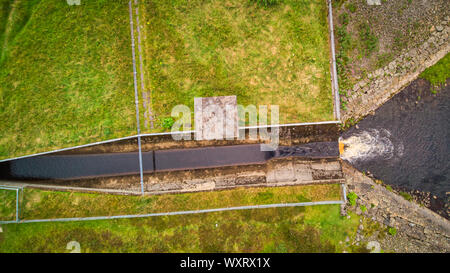 Luftaufnahme einer Entlastungsanlage, Loch Revolver Behälter Dam. Blaue Wasser fließt zwischen grünen Feldern Stockfoto