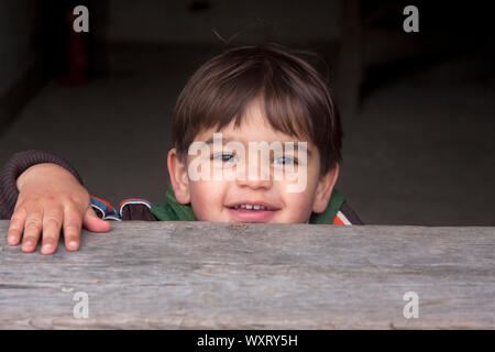 Happy little boy Peering über hölzernen Türrahmen Stockfoto