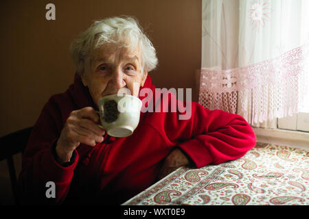 Porträt eines alten grauhaarige Frau, trinken Tee an seinem Haus. Stockfoto