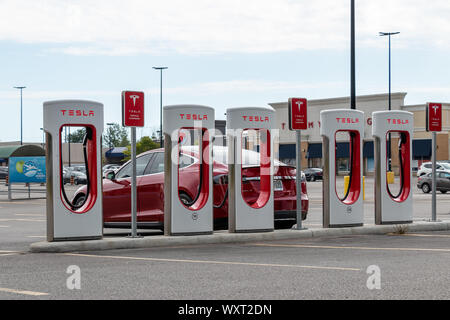 Tesla Supercharger Station auf offenem Parkplatz mit Tesla Model S dahinter eingesteckt. Stockfoto