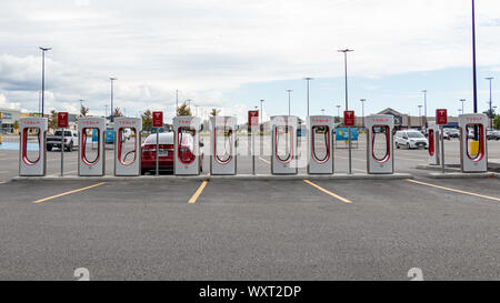 Tesla Supercharger auf einem Parkplatz im Einkaufszentrum mit Auto-Ladefunktion hinten. Stockfoto