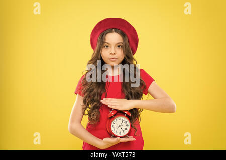 Kind mit Wecker. Zeitlose Mode Beauty Friseur. Pariser Kind auf gelben Hintergrund. nettes Mädchen mit langen Locken in Baskenmütze. Kleines Mädchen im französischen Stil hat. Moderne und Retro Mode. Stockfoto