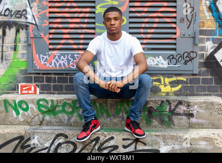 Ein junger Mann stellt auf einigen Schritten mit grafitti Mauer im Hintergrund auf einer Straße der Stadt in Shoreditch Stockfoto