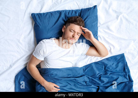 Bedtime. Guy liegend auf Bett oben berühren Kopf Kopfschmerzen Stockfoto