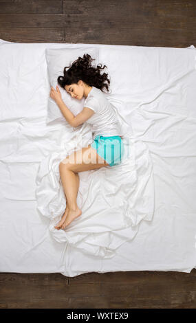 Junge Frau auf dem Bett Top View hugging Pillow Stockfoto