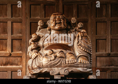 DEC 3, 2018 Yamagata, Japan - Japanische geschnitztem Holz lächelnden Buddha Statue mit altem Holz Wand in Yamadera Risshaku ji Temple Stockfoto