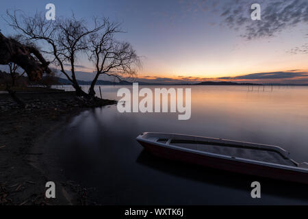 Ein leeres kleines Boot in See Trasimeno (Umbrien, Italien) in der Abenddämmerung, in der Nähe von einem Skelett Baum Stockfoto