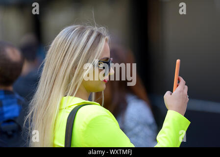 Junge Frau in hellem Gelb mit Orange Handy bei der London Fashion Week, 2019. Stockfoto