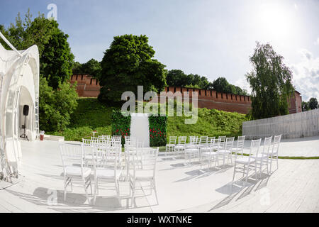 Reihen von leeren, weißen Stühlen sitzen auf einem Holzboden. Hochzeit Stühle mit Blumen an Zeremonie im Freien Stockfoto