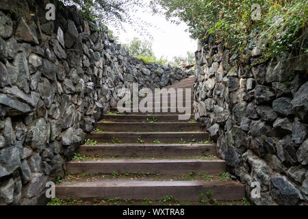 Eine lange, hohe Treppe mit Holzstufen Verlängerung nach oben von Steinmauern umgeben. Reisen und mystische Orte. Stockfoto