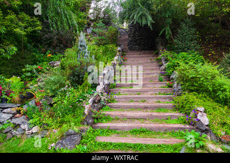 Eine lange, hohe Treppe mit Holzstufen Verlängerung nach oben durch Steine und grünen Pflanzen im Sommer im Garten umgeben. Reisen und mystische Orte. Stockfoto