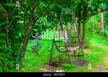 Eine alte Retro wrought Eisen metall Swing mit einer Holzbank im Vintage Style steht in einem Garten oder Park für Kinder Unterhaltung, Entspannung und d Stockfoto