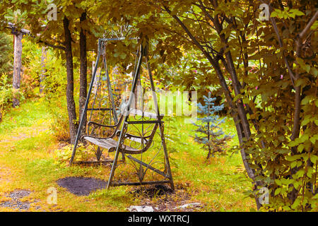 Eine alte Retro wrought Eisen metall Swing mit einer Holzbank im Vintage Style steht in einem Garten oder Park für Kinder Unterhaltung, Entspannung und d Stockfoto