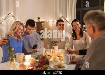 Familie, Urlaub und Personen Konzept - glückliches Paar mit Smartphone in Tea Party zu Hause Stockfoto