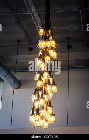 Eine Gruppe von industriellen Lampen mit gelben Glühbirnen dekorativ hängen als Bundle leuchten auf eine konkrete Oberfläche mit Bereich für Werbung Stockfoto