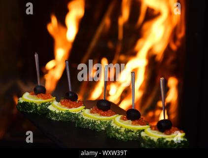 Kalte Vorspeisen, canape mit rotem Kaviar, Feuer für den Hintergrund. Leckere Snacks serviert im Restaurant auf schwarze Küche. Mit oliven, roter Kaviar Canape, le Stockfoto