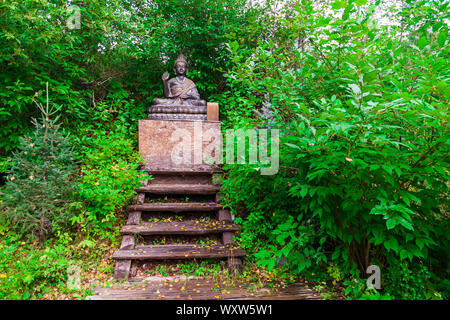 Buddha Statue sitzend in Lotus Position für Anbetung und Meditation der Buddhisten in einer blühenden, grünen Garten mit grünen Bäumen und Blättern. Religion und Stockfoto