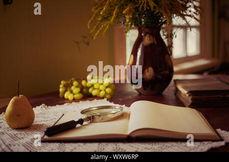 Alte Bücher auf einem Holztisch und Glaslupe. Stockfoto