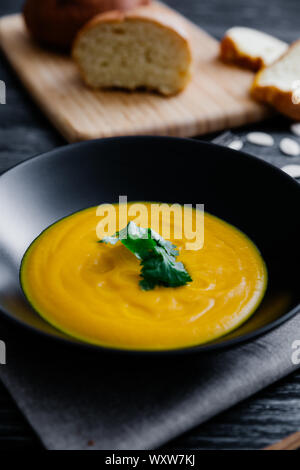 Kürbissuppe serviert in einem hellen Schüssel mit Brot Petersilie und Kürbiskerne Stockfoto