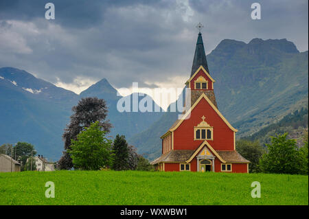 Rote hölzerne Kirche in Olden, Stryn im Oldedalen Tal, Norwegen. Schöne Szene, grüne Wiese, bergigen Landschaft, stürmischen Himmel Stockfoto