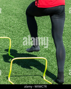 Ein Athlet Socken tragen verstärkt über Gelb mini Hürden, die Beweglichkeit und Form Bohrer für Running Socken tragen. Stockfoto