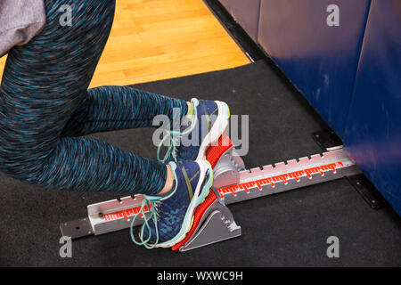 Ein Sprinter, Sprint start Praxis mit den Start in der Nacht in der High School Turnhalle im Winter Leichtathletik Saison. Stockfoto