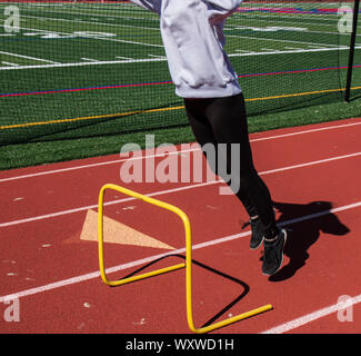 Ein High School track Athlet ist Zoll vom Boden an, als sie über eine gelbe 2 Fuß Hürde bei der Geschwindigkeit und Agilität der Praxis auf einem roten Titel springt. Stockfoto