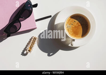 Schale, Notepad und Sonnenbrille auf dem weißen Tisch an einem sonnigen Tag. Moderne trendige Flach mit Tageslicht Stockfoto