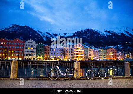 Innsbruck bei Nacht, farbenfrohen alten Gebäude, in den Fluss reflektiert, bahndamm mit Fahrrädern, Alpen mit Schnee bedeckt, Tirol, Österreich. Stockfoto