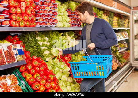 Junger Mann mit Warenkorb während des Einkaufs in der Gemüseabteilung im Supermarkt Stockfoto