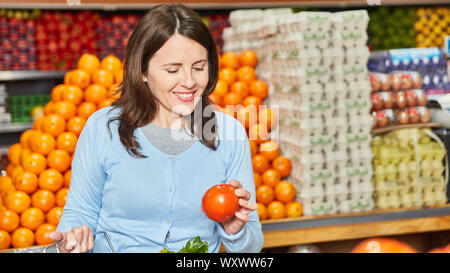 Lächelnde Frau als Kunden frische Bio Tomaten in der Gemüseabteilung kauft Stockfoto