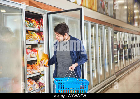 Kunden im Supermarkt steht an gefrorene Lebensmittel im Kühlschrank Regal und sieht einen Pack von Pommes frites Stockfoto