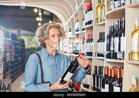 Kunden im Supermarkt vor dem Regal mit einer Flasche Rotwein in der Hand Stockfoto