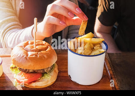 Woman's Hand, ein Pommes Frites. Prozess der Burger essen und Pommes frites close-up Stockfoto