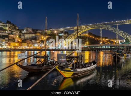 Rabelo Boote verwendet Port in Porto in Portugal mit einem Panorama auf die Skyline der Altstadt zum Transport in der Nacht mit Beleuchtung im Fluss spiegeln Stockfoto