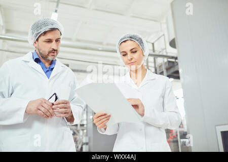 Zwei Technologen in Laborkittel und Masken in der Fabrik. Stockfoto