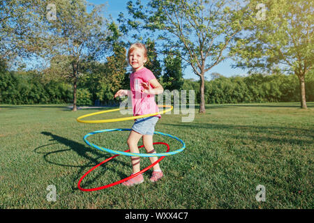 Nett Lächeln, Kaukasier Vorschule blonde Mädchen spielen mit hoola Hoop in Park draußen auf Sommertag. Kinder Sport. Lifestyle glücklich Stockfoto