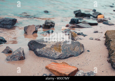 Kiesel auf einem sandigen Ufer in klares Wasser. Die seidigen Wellen eines blauen See schlug die Steine. Natürliche Hintergrund. Stockfoto