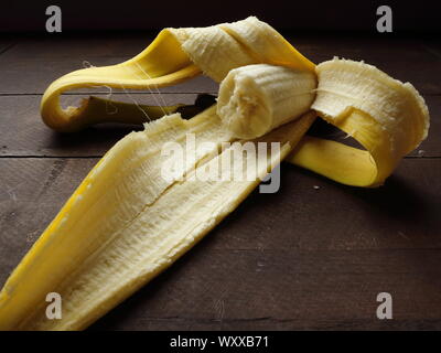 Teilweise Banane noch in der Schale auf rustikalen Holztisch gegessen Stockfoto