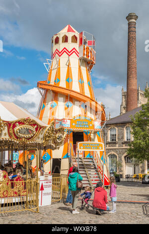 Ein Helter Skelter messe Fahrt auf Anker Square im Stadtzentrum von Bristol mit Rowes Leadworks Schornstein an der Rückseite, Avon, England, UK. Stockfoto