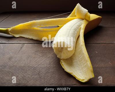 Teilweise Banane noch in der Schale auf rustikalen Holztisch gegessen Stockfoto