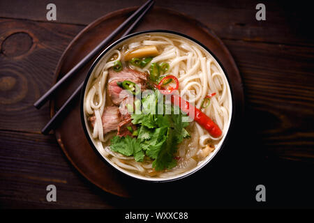 Traditionelle vietnamesische Suppe Pho Bo mit Rindfleisch und mit frischem Koriander auf dunklem Hintergrund Stockfoto