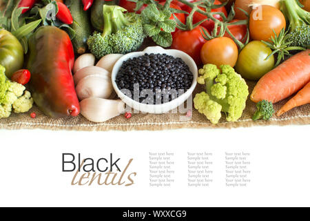 Ungekocht schwarze Linsen in eine Schüssel mit Gemüse isoliert auf weißem Stockfoto