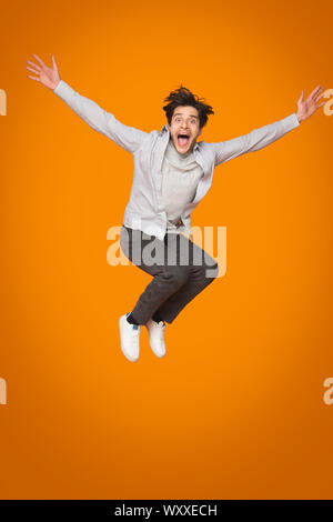 Crazy man springen mit erhobenen Armen über orange Hintergrund Stockfoto