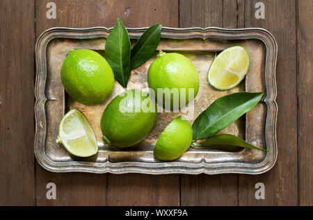 Frische Limetten mit Blätter auf einem silbernen Tablett auf einem Holztisch Stockfoto