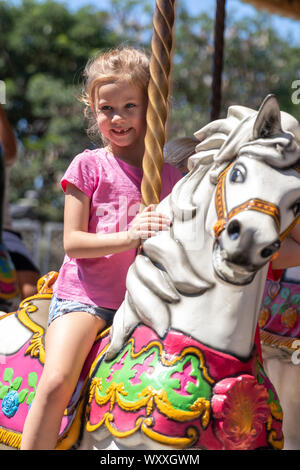 Süße kleine Mädchen reiten auf einem Karussell in einen Vergnügungspark im Sommer. Stockfoto