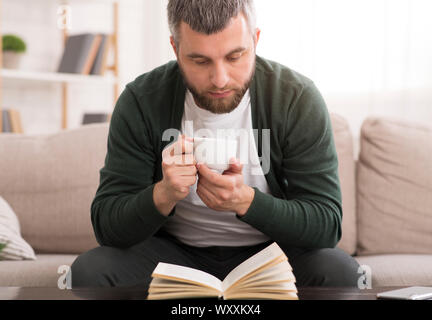 Bärtiger Mann trinkt Kaffee beim Lesen Buch Stockfoto