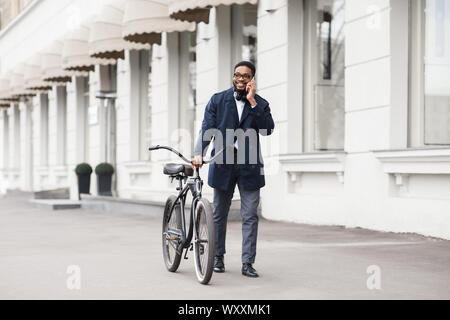 Afro Geschäftsmann zu Fuß, mit dem Fahrrad und am Telefon sprechen Stockfoto